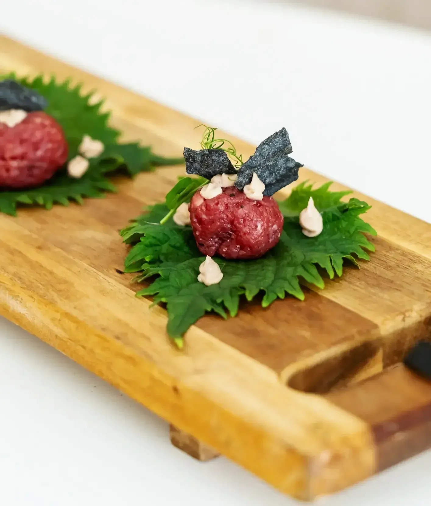 Steak tartaar met houtskoolcracker op shiso-blad, op een houten plank