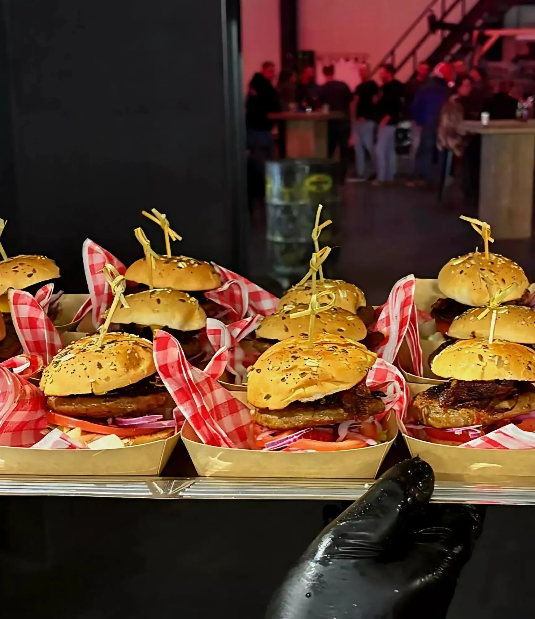 Sliders in ruitjespapier in houten bakjes, avondlicht met gasten op de achtergrond