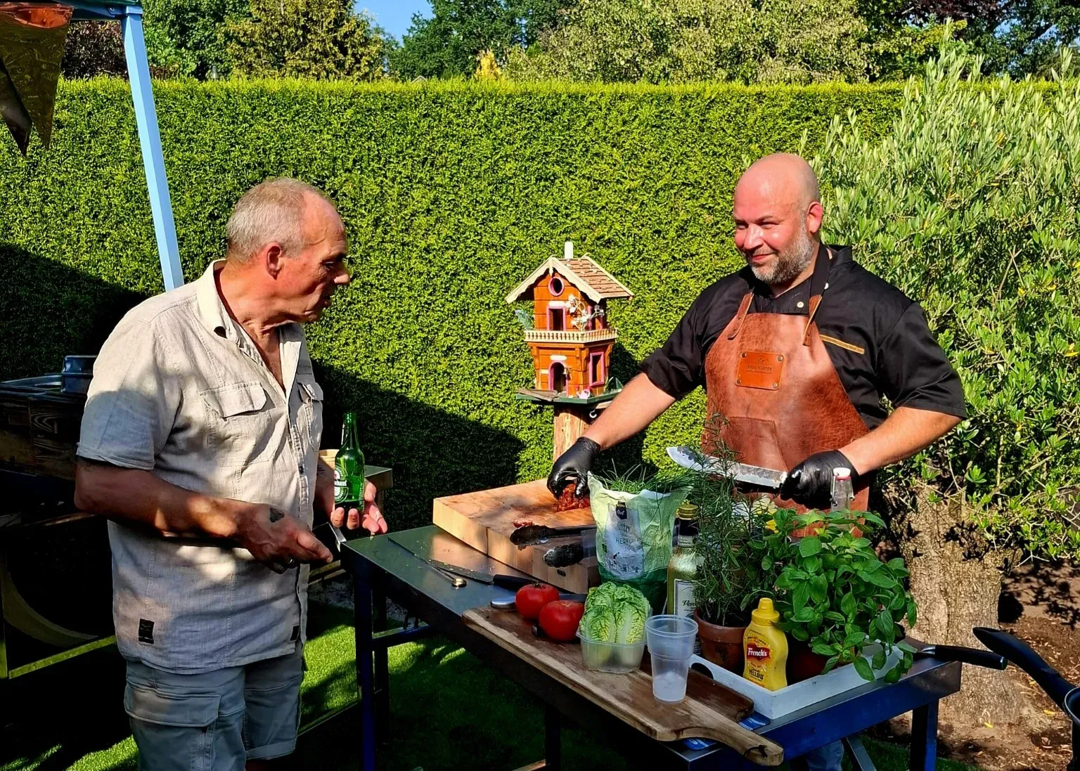 Berry en de gastheer aan een preptafel met kruiden en drankjes in de tuin